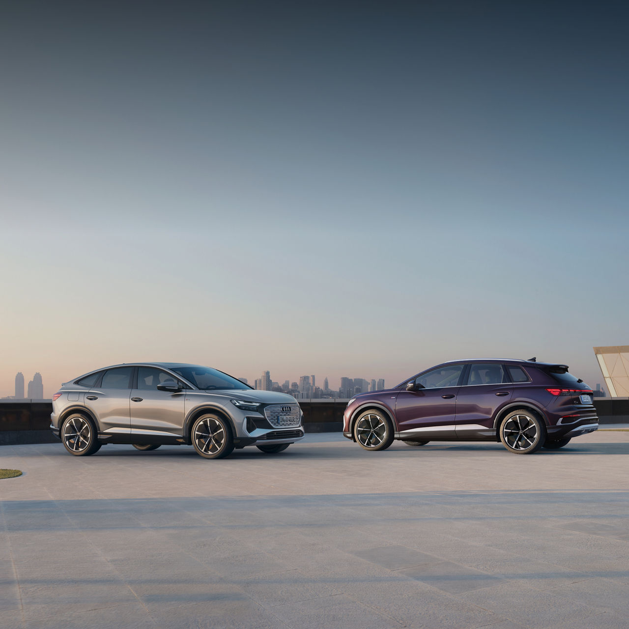 Two parked Audi electric vehicles parked and facing each other with a cityscape in the distance